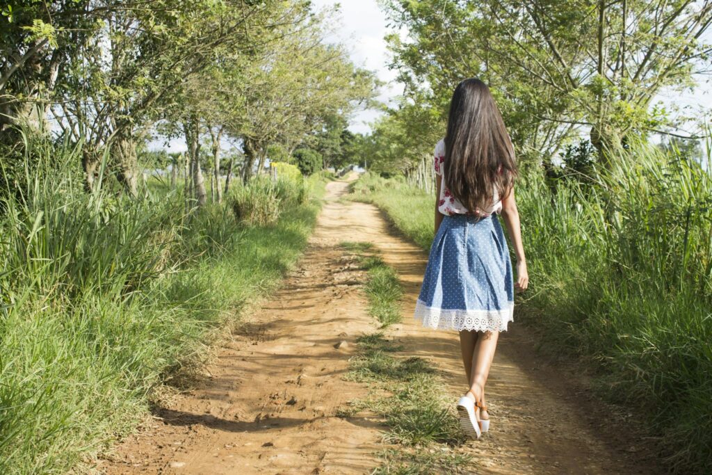Woman Wearing Blue and White Skirt Walking Near Green Grass during Daytime
